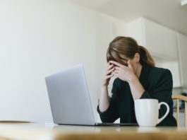Woman sitting across from laptop with hands over her eyes - Actions to overcome job search blues