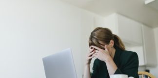 Woman sitting across from laptop with hands over her eyes - Actions to overcome job search blues