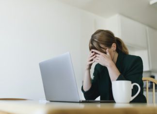 Woman sitting across from laptop with hands over her eyes - Actions to overcome job search blues